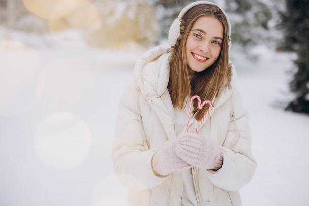 Une jolie fille en mitaines tricotées tient des cannes de bonbons sous la forme d'un cœur dans le parc d'hiver - Photo, image