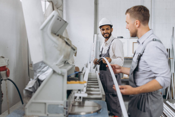Uma equipe internacional, dois trabalhadores trabalham em uma máquina em uma fábrica de janelas e portas de PVC - Foto, Imagem