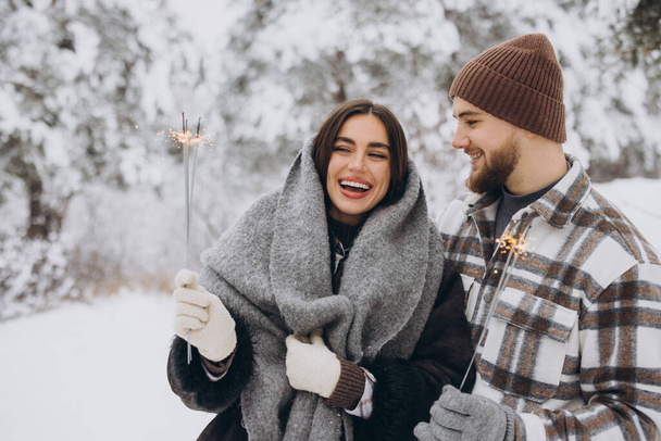 Hymyilevä romanttinen pari neulottu hatut poseeraa Sparklers talvimetsässä, pitämällä Bengal valot käsissä, juhlii joulun lomat yhdessä, Kopioi tilaa - Valokuva, kuva
