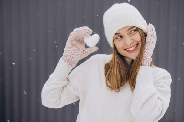 Happy woman in knitted mittens holding a snow heart on a winter snowy day - Photo, Image