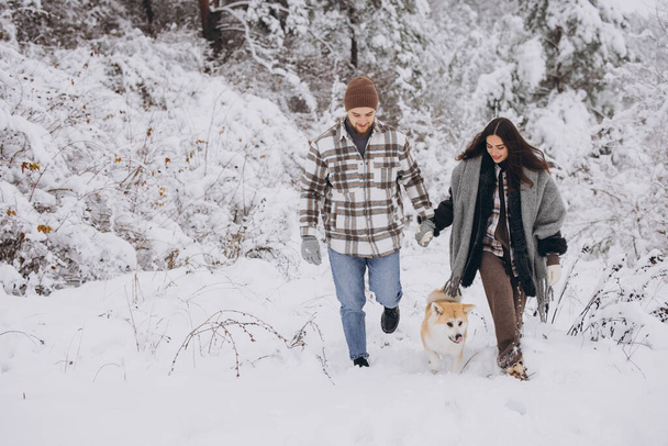 Счастливая молодая пара с акита-собакой в лесу в зимний и снежный день - Фото, изображение