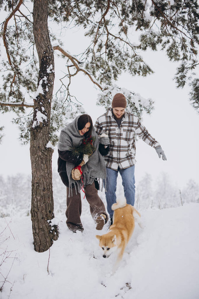 Ευτυχισμένο νεαρό ζευγάρι με σκύλο ακίτα στο δάσος την ημέρα του χειμώνα - Φωτογραφία, εικόνα