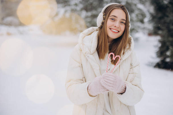 編まれたミトンのかわいい女の子は冬の公園で心臓の形でキャンディー缶を保持します - 写真・画像