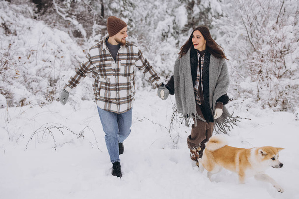 Feliz pareja joven con un perro akita en el bosque en invierno y día nevado - Foto, Imagen