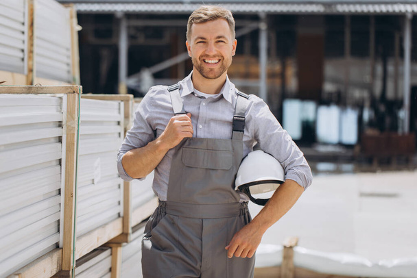 Een manager of medewerker in een grijs speciaal uniform en een witte harde hoed staat glimlachend in de buurt van lading voor export of import. - Foto, afbeelding