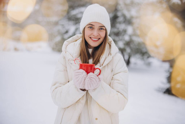 Aranyos boldog nő kötött kesztyűben tartja forró kávé cukornád a téli parkban - Fotó, kép