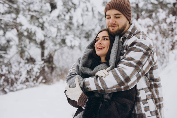 Ένα νεαρό ευτυχισμένο και αξιαγάπητο ζευγάρι διασκεδάζει σε ένα χιονισμένο δάσος το χειμώνα.. - Φωτογραφία, εικόνα
