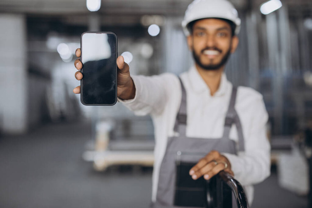 Portré boldog hindu munkavállaló fehér kemény kalap és overál gazdaság smartphone és mutatja üres képernyő másolatot gyári háttér. - Fotó, kép