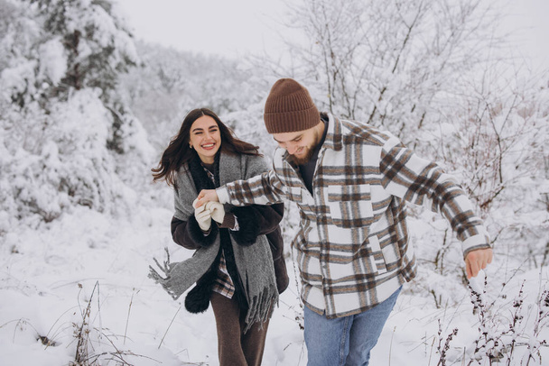 Młoda szczęśliwa i kochająca się para spacerująca po zaśnieżonym lesie w górach - Zdjęcie, obraz