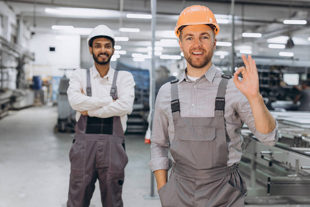 Two international male workers in overalls on the background of the production of PVC windows and doors - Photo, Image