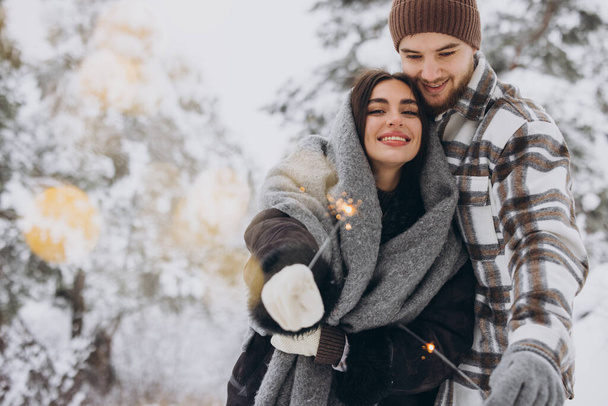 Sorridente coppia romantica in maglia cappelli in posa con scintille a foresta invernale, Tenere le luci del Bengala nelle mani, Celebrare le vacanze di Natale insieme, Copia spazio - Foto, immagini