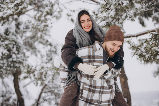 Młoda szczęśliwa i kochająca się para bawi się w śnieżnym lesie zimą. - Zdjęcie, obraz