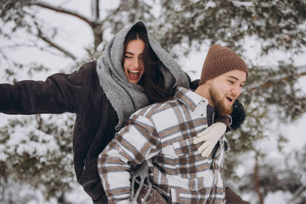 Ein junges glückliches und liebevolles Paar vergnügt sich im Winter im verschneiten Wald. - Foto, Bild