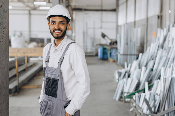 Retrato de um trabalhador indiano feliz em um uniforme cinza e um chapéu branco posando no fundo da produção da fábrica - Foto, Imagem
