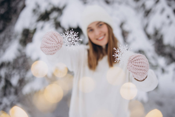 Happy woman in knitted white clothes holding snowflakes on the background of a snowy pine tree in winter - Photo, Image