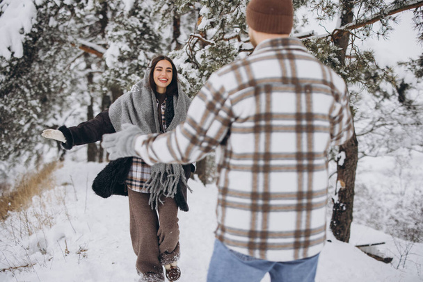 山の冬の雪の森を歩く若い幸せで愛するカップル - 写真・画像