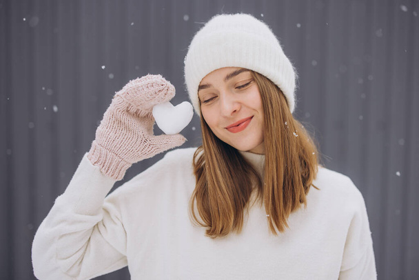 Happy woman in knitted mittens holding a snow heart on a winter snowy day - Photo, Image