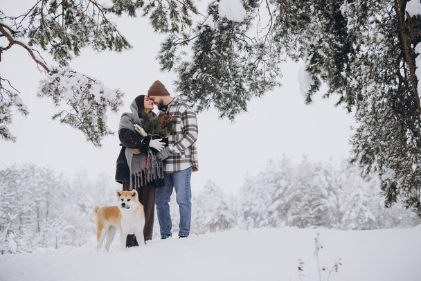 Feliz pareja joven con un perro akita en el bosque en el día de invierno - Foto, imagen