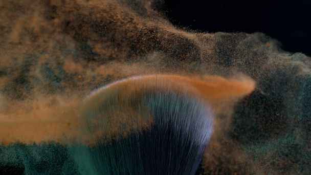 Makro-Nahaufnahme eines kosmetischen Pinsels, der in Superzeitlupe aufeinanderprallt, aufgenommen mit einer Hochgeschwindigkeitskamera bei 1000 fps mit orangefarbenem und grünem Pulver, das in der Luft fliegt - Foto, Bild