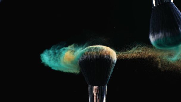 Maquiagem escova tocando com partículas cosméticas em movimento super lento em fundo escuro - Foto, Imagem