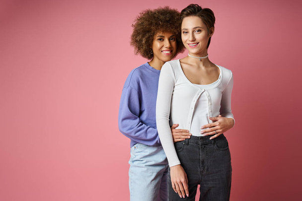 радісні багатокультурні лесбіянки, що обіймаються, стоячи на рожевому фоні, пара lgbtq - Фото, зображення