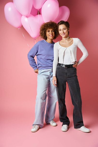 счастливая межрасовая лесбийская пара улыбается около розовых шаров в форме сердца, День Святого Валентина - Фото, изображение