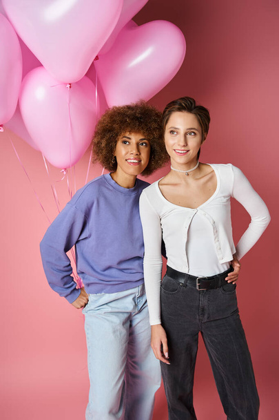 dreamy multicultural lesbian couple smiling near pink heart shaped balloons, Saint Valentines day - Zdjęcie, obraz