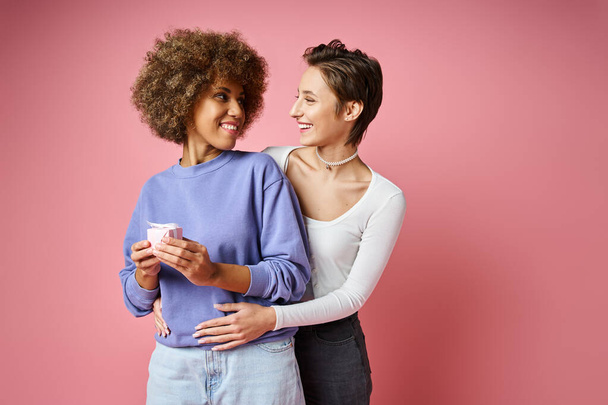 cheerful lesbian woman looking at happy african american girlfriend with present on Valentins day - Photo, Image