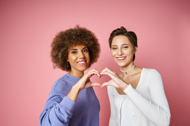 幸せな多文化とレズビアンのカップルは,ピンクの背景に手でハートサインを示しています, lgbtq愛 - 写真・画像