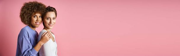 портрет молодої багатокультурної пари lgbtq в повсякденному одязі, дивлячись на камеру на рожевому, банер - Фото, зображення