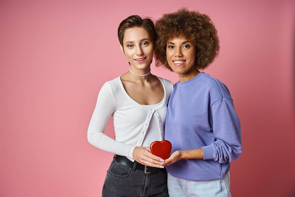 joyful multicultural lgbtq couple holding red heart shaped box on pink background, Valentines day - Photo, Image
