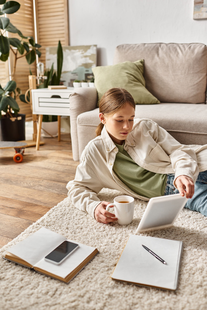 dospívající dívka drží tablet a šálek čaje, zatímco její domácí úkol, digitální rodný koncept - Fotografie, Obrázek