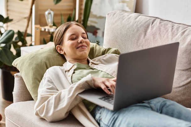 veselá dospívající dívka pomocí svého notebooku a ležící na pohodlné pohovce doma, dálkové vzdělávání - Fotografie, Obrázek