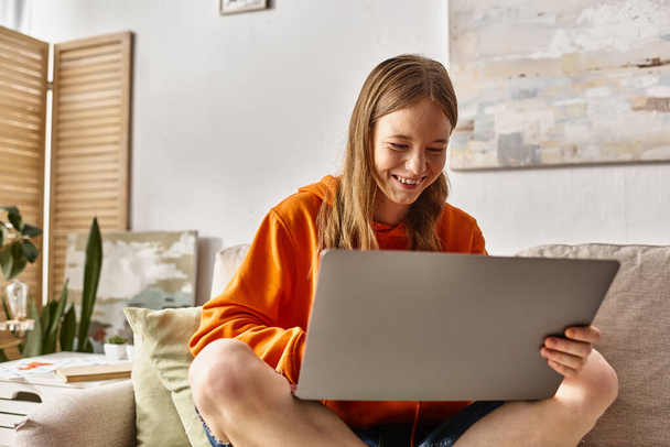 heureux adolescent fille avec un ordinateur portable profiter de son temps et assis sur le canapé dans le salon - Photo, image