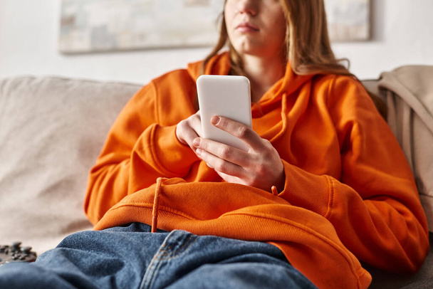 recortado disparo de adolescente utilizando su teléfono inteligente y sentado en el sofá en la sala de estar, medios de comunicación social - Foto, imagen