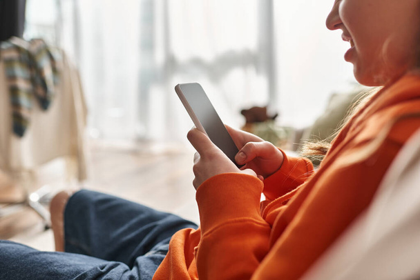 обрізана щаслива дівчина-зоомер використовує свій смартфон і сидить на дивані у вітальні, користувач соціальних мереж - Фото, зображення