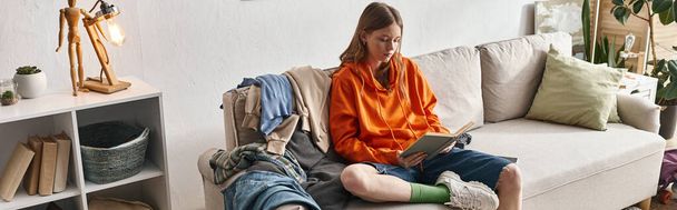 Teenager-Mädchen liest Buch, während sie auf chaotischem Sofa neben Kleiderstapel in der Wohnung sitzt, Banner - Foto, Bild
