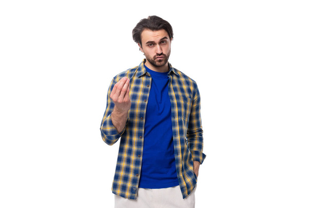 charmante goed verzorgde brunette macho man met een baard en snor in een blauw shirt op een witte achtergrond met kopieerruimte. - Foto, afbeelding