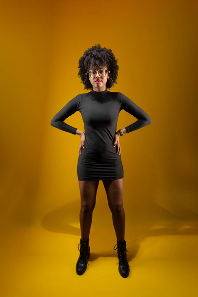 Sensuelle jeune femme debout, portant des vêtements noirs et posant pour une photo. Isolé sur fond jaune. - Photo, image