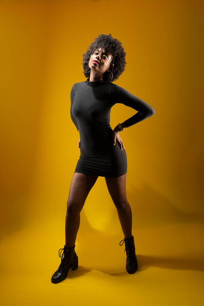 Чуттєва молода жінка стоїть, носить чорний одяг і позує на фото. Ізольовані на жовтому тлі. - Фото, зображення