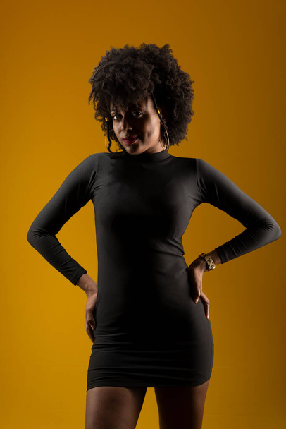 Smyslná mladá žena, oblečená v černém a pózující na fotografii. Izolováno na žlutém pozadí. - Fotografie, Obrázek
