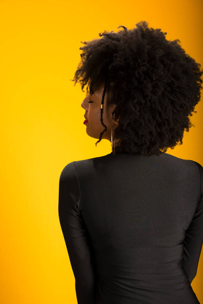 Sensuale donna bruna con i capelli neri potere di fronte alla fotocamera. Isolato su fondo giallo. - Foto, immagini