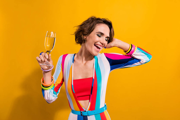Photo of carefree funky lady wear striped costume dancing drinking champagne isolated yellow color background. - 写真・画像