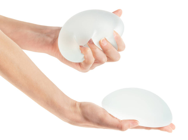 Female squeezing soft breast implant in hand on white background. Aesthetic surgery. - Photo, Image