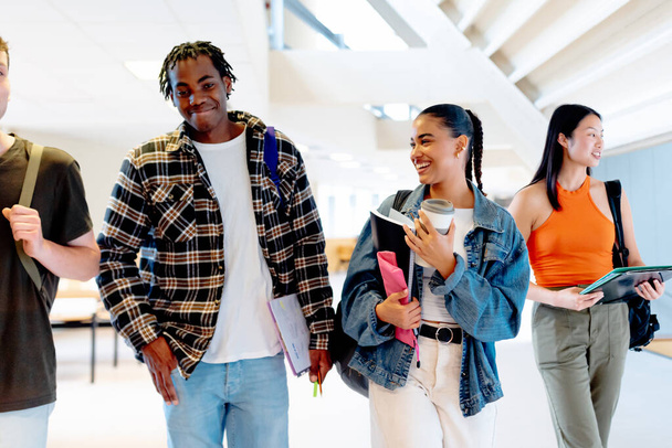 Multiraciale groep jonge studenten die met schoolspullen door de hallen van de universiteitscampus of de middelbare school lopen. - Foto, afbeelding