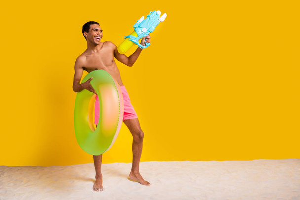 Full length photo of cute funny shirtless man holding floating ring showing water empty space isolated yellow color background. - Foto, imagen