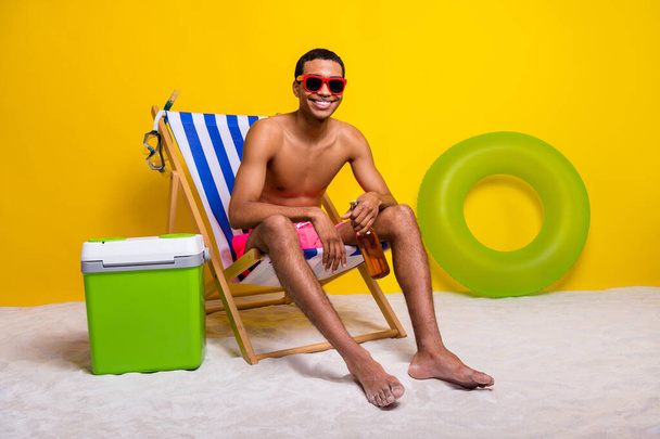 Full length photo of good mood positive shirtless man having rest lounge chair drinking beer isolated yellow color background. - Foto, immagini