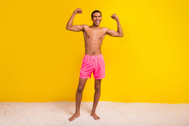 Full length photo of excited lucky shirtless man showing arms muscles isolated yellow color background. - Fotografie, Obrázek