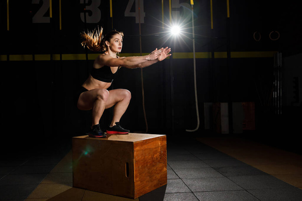 Donna atletica in abbigliamento sportivo che salta sulla scatola crossfit in palestra fitness. Stile di vita sano - Foto, immagini