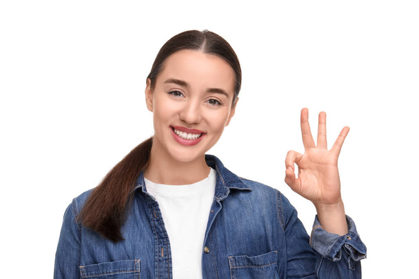 Young woman with clean teeth smiling and showing ok gesture on white background - Fotó, kép